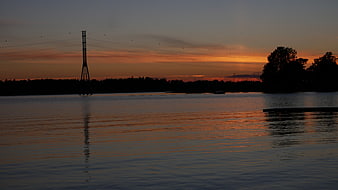 Silhouette of Power Lines and Trees Over Calm River at Sunset