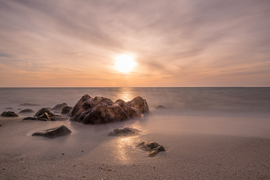 Serene Sunset Over Misty Ocean Rocks and Sandy Beach