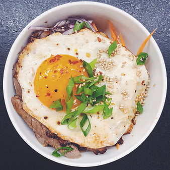Overhead view of beef donburi with fried egg and green onions
