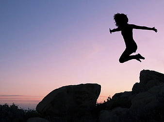 Silhouette of Woman Jumping on Rocks at Sunset