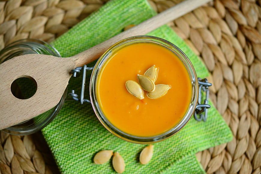 Overhead view of creamy pumpkin soup in a glass jar with seeds