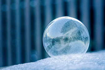 Frosted Ice Sphere on Snowy Surface with Blue Bokeh Background