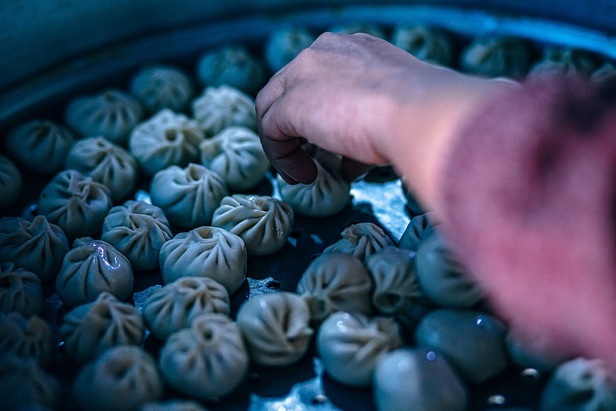 Hand Placing Steamed Dumplings In Traditional Bamboo Steamer