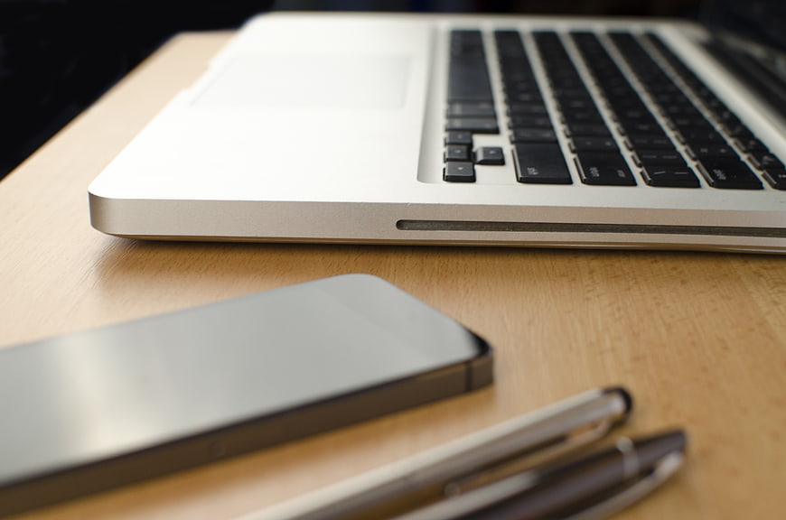 Modern workspace with laptop, smartphone, and pens on wooden desk