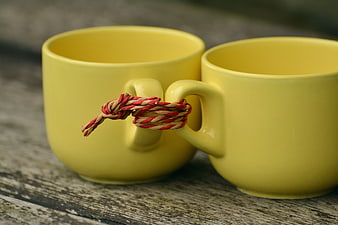 Two yellow mugs tied together with red and beige rope on rustic wood