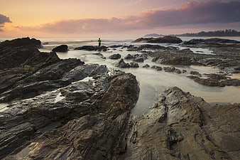Lone Figure Standing on Rocky Coastline at Sunset