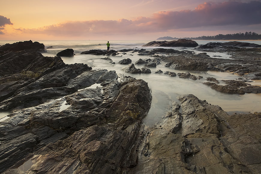 Lone Figure Standing on Rocky Coastline at Sunset
