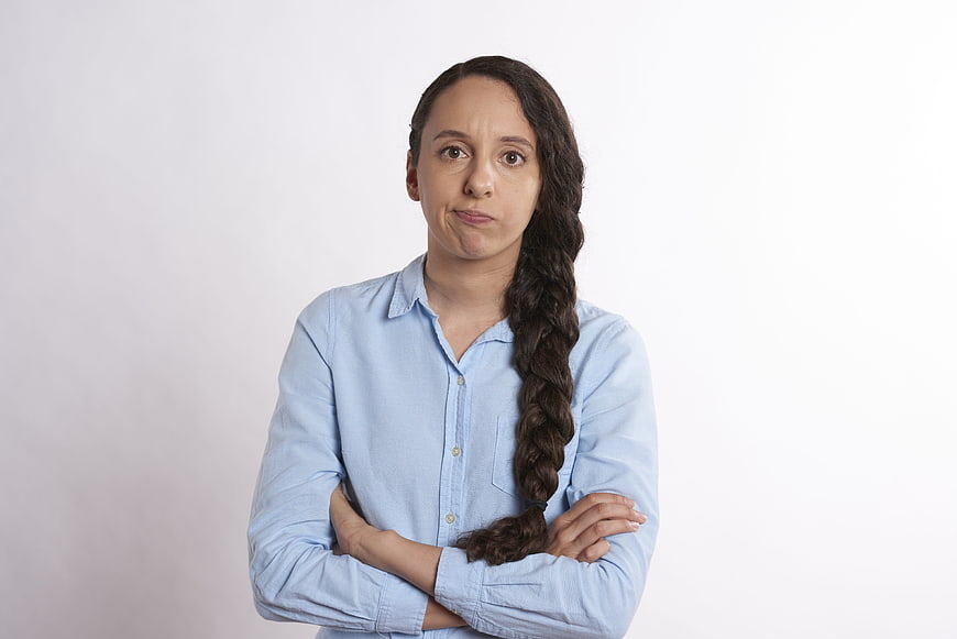 Frustrated woman with crossed arms and long braid on white background