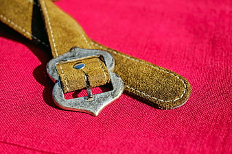 Close-up of brown leather belt with metal buckle on red fabric