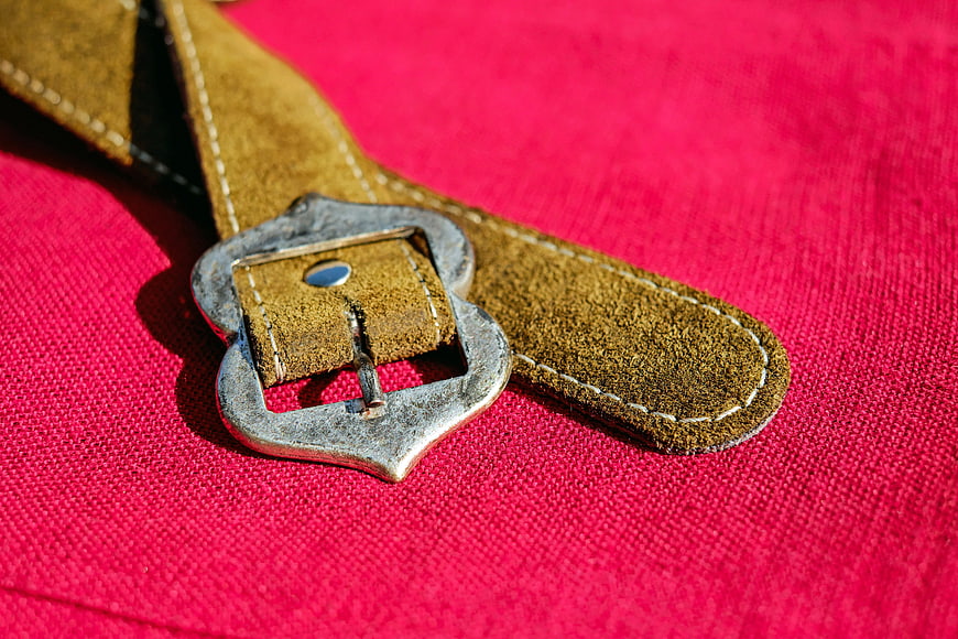 Close-up of brown leather belt with metal buckle on red fabric