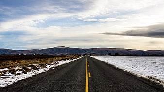 Winter Highway Stretching to Distant Mountains Under Cloudy Sky