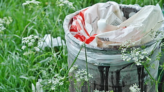Overflowing trash bin in grass with plastic waste