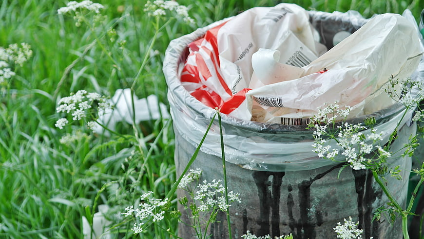 Overflowing trash bin in grass with plastic waste