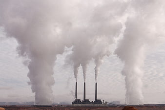 Industrial smokestacks emitting thick white smoke into the sky