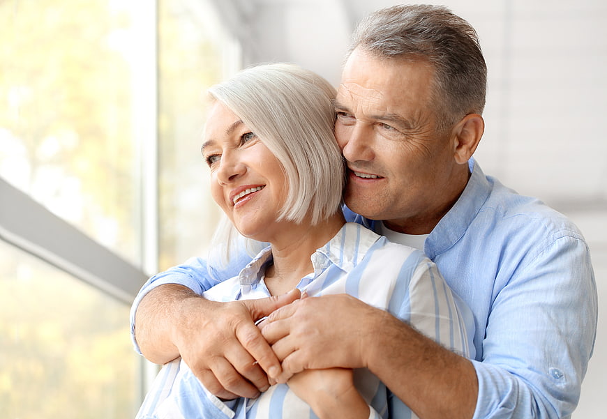 Happy senior couple embracing by window