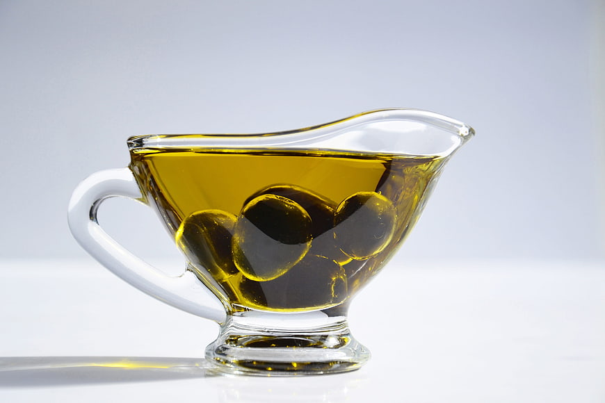 Glass gravy boat with olive oil and olives on white background