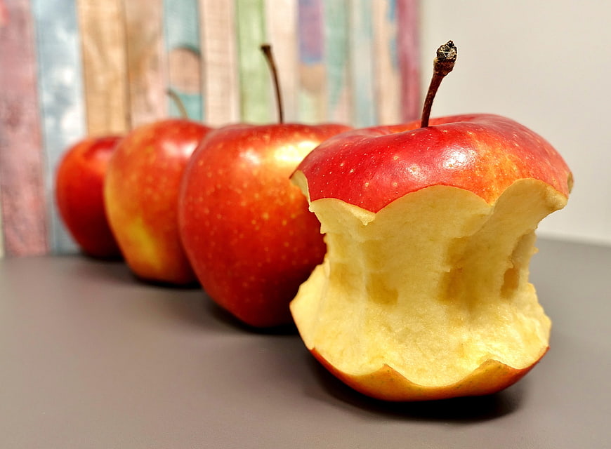 Bitten Red Apple In A Row With Blurred Book Background