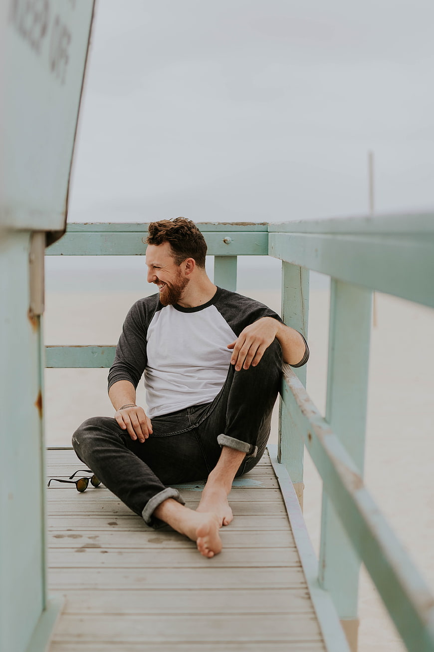 Happy bearded man sitting on wooden pier by the beach
