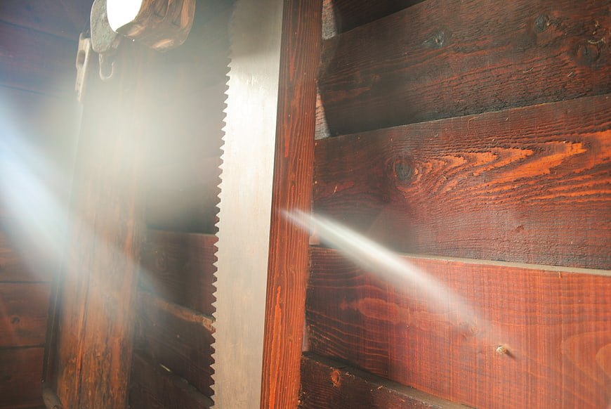 Vintage hand saw hanging on rustic wooden wall with sun flare