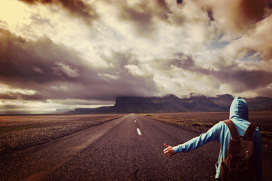 Hitchhiker on desolate highway under dramatic cloudy sky