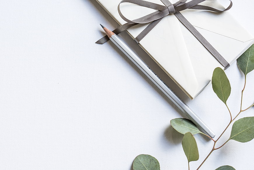 Minimalist white gift box with ribbon, pencil, and eucalyptus leaves