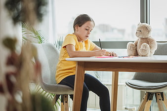 Young girl doing homework at table with teddy bear