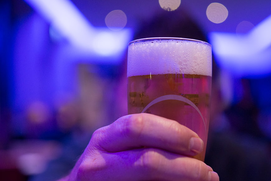 Hand Holding Beer Glass in Blue Lit Bar