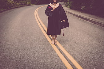 Female graduate in black gown walking on road