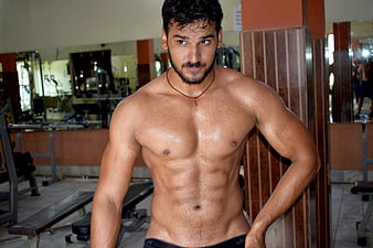 Muscular shirtless man with defined abs in a gym