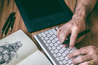 Digital artist hands typing on keyboard with graphics tablet and sketchbook
