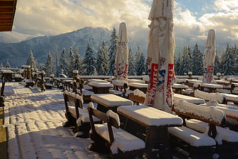 Snow-covered mountain terrace with wooden tables and closed umbrellas
