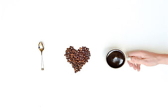 Flat lay of coffee beans heart, spoon, and cup on white background