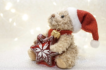 Cute teddy bear in Santa hat holding red star Christmas ornament