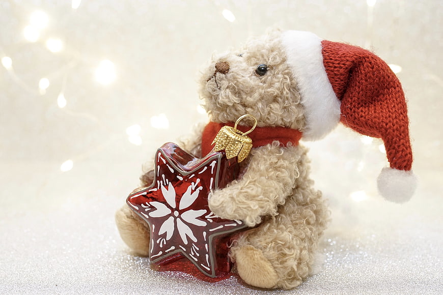 Cute teddy bear in Santa hat holding red star Christmas ornament