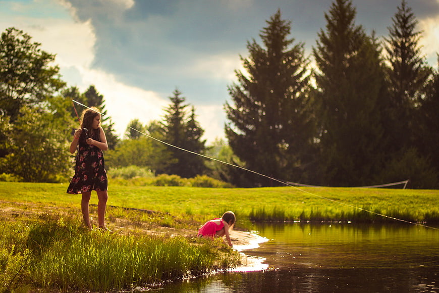 Two young girls playing by a lake in a sunny meadow