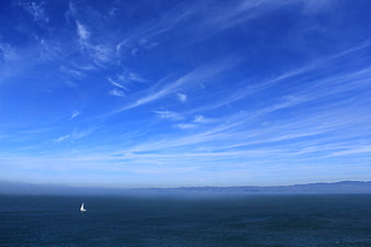 Lone Sailboat on Ocean Under Blue Sky with Wispy Clouds