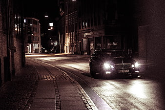 Black SUV Driving On Wet Cobblestone Street At Night