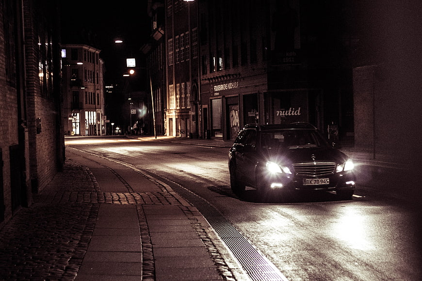 Black SUV Driving On Wet Cobblestone Street At Night