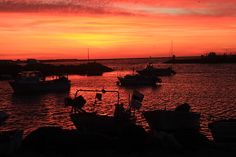 Silhouetted Fishing Boats in Harbor at Vibrant Red Sunset