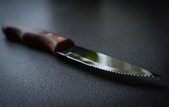 Close-up of a serrated steak knife on a dark textured surface