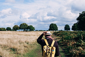Man with yellow backpack walking on path in field