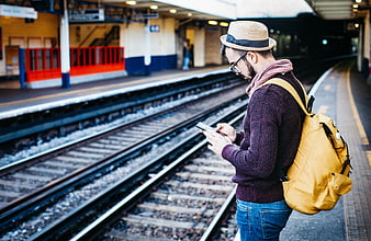 Man with backpack checking smartphone at train station platform