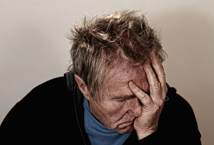 Senior man holding head in despair and exhaustion