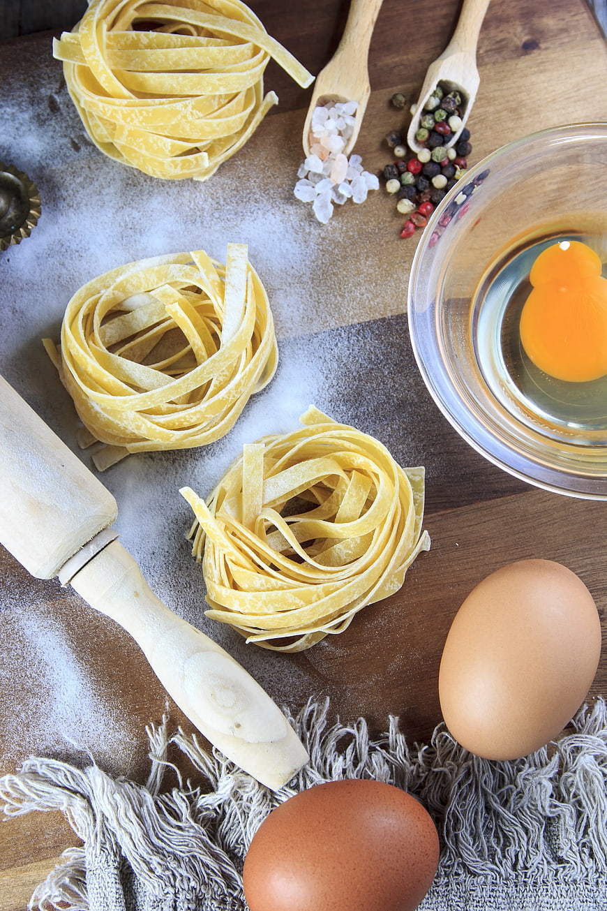 Fresh handmade pasta nests with eggs and flour on wooden table