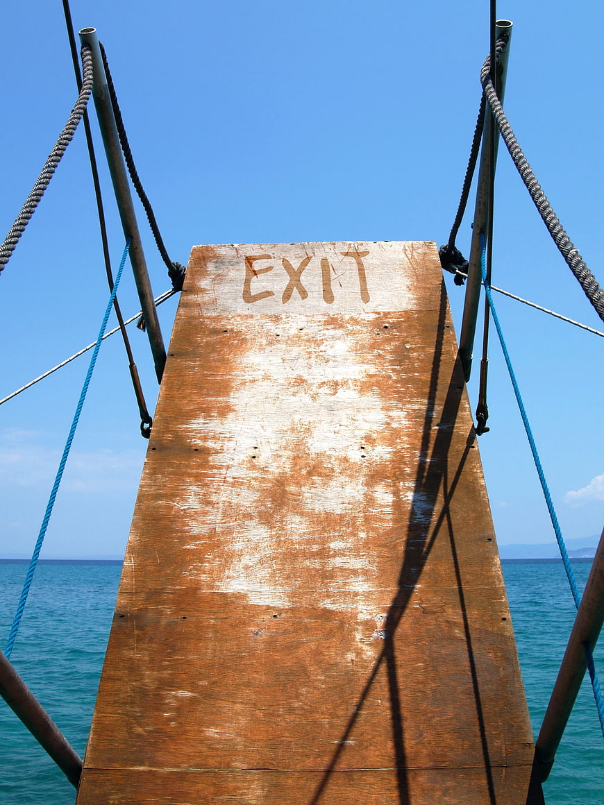 Wooden exit sign on boat ramp leading to blue ocean
