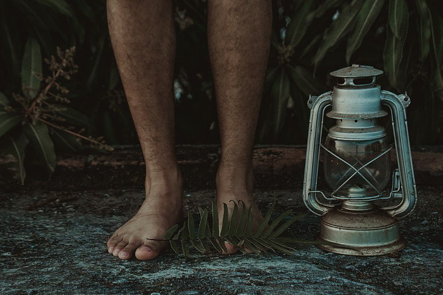 Bare feet standing next to vintage lantern on concrete
