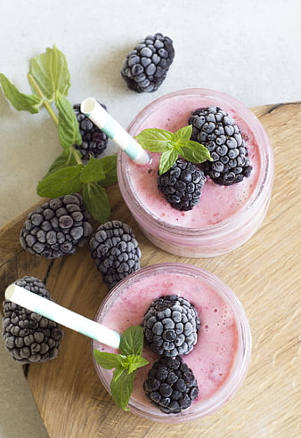 Two blackberry smoothies in glass jars with mint garnish on wooden board