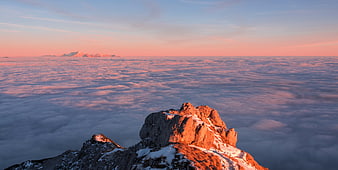Sunlit mountain peak above sea of clouds at sunrise