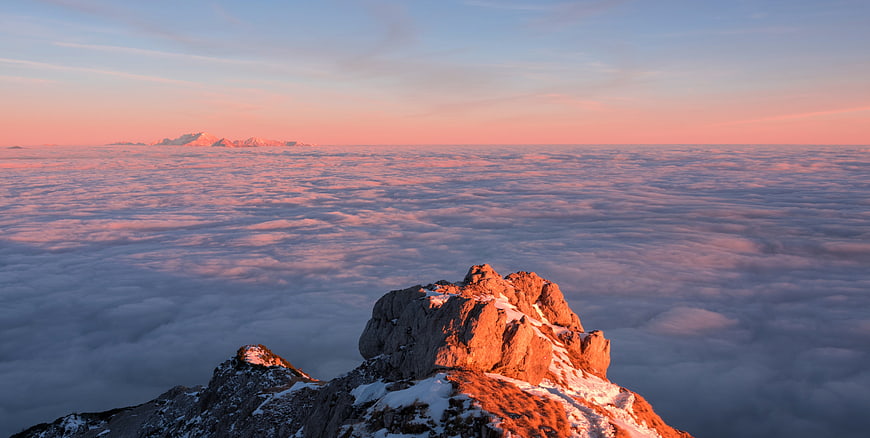 Sunlit mountain peak above sea of clouds at sunrise