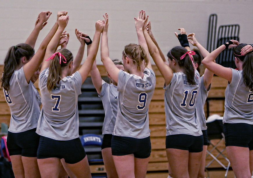 Female volleyball team huddle with arms raised in celebration